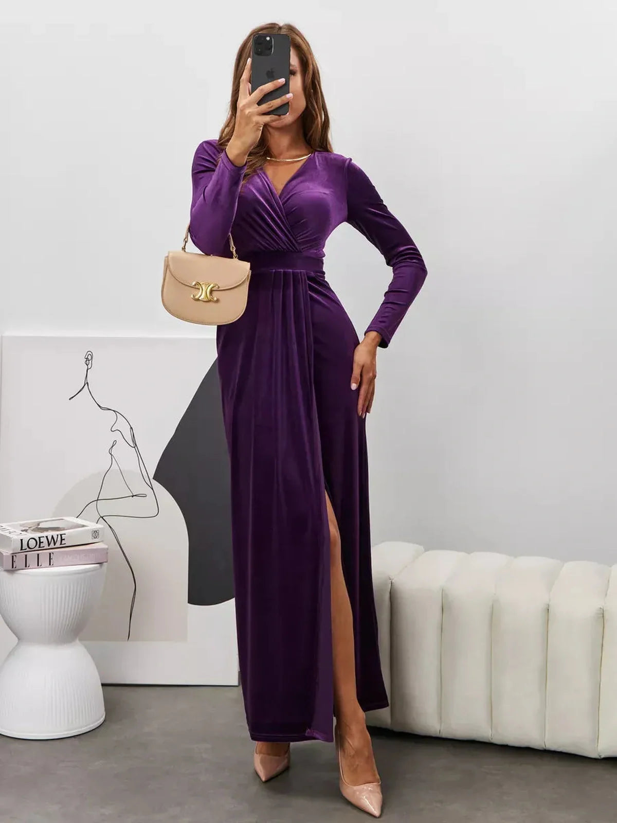 Woman in a Plum Aura Maxi Dress featuring a deep V-neck, long sleeves, and a sultry slit, holding a handbag.