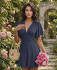 Elara Mini Dress in navy with V-neckline and flutter sleeves, paired with a woven bag and flowers, by Lauven.