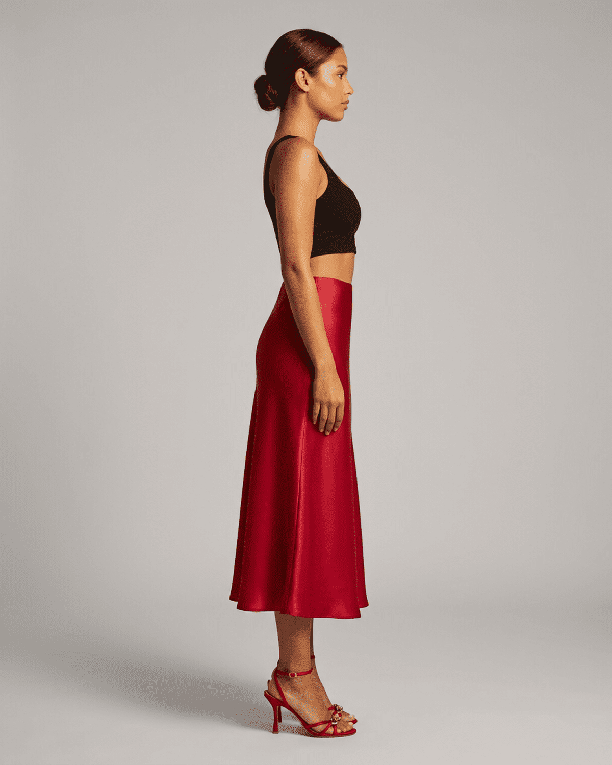 Side view of a woman wearing the Rosalia Midi Skirt by Lauven in rich red satin, showcasing its elegant silhouette.