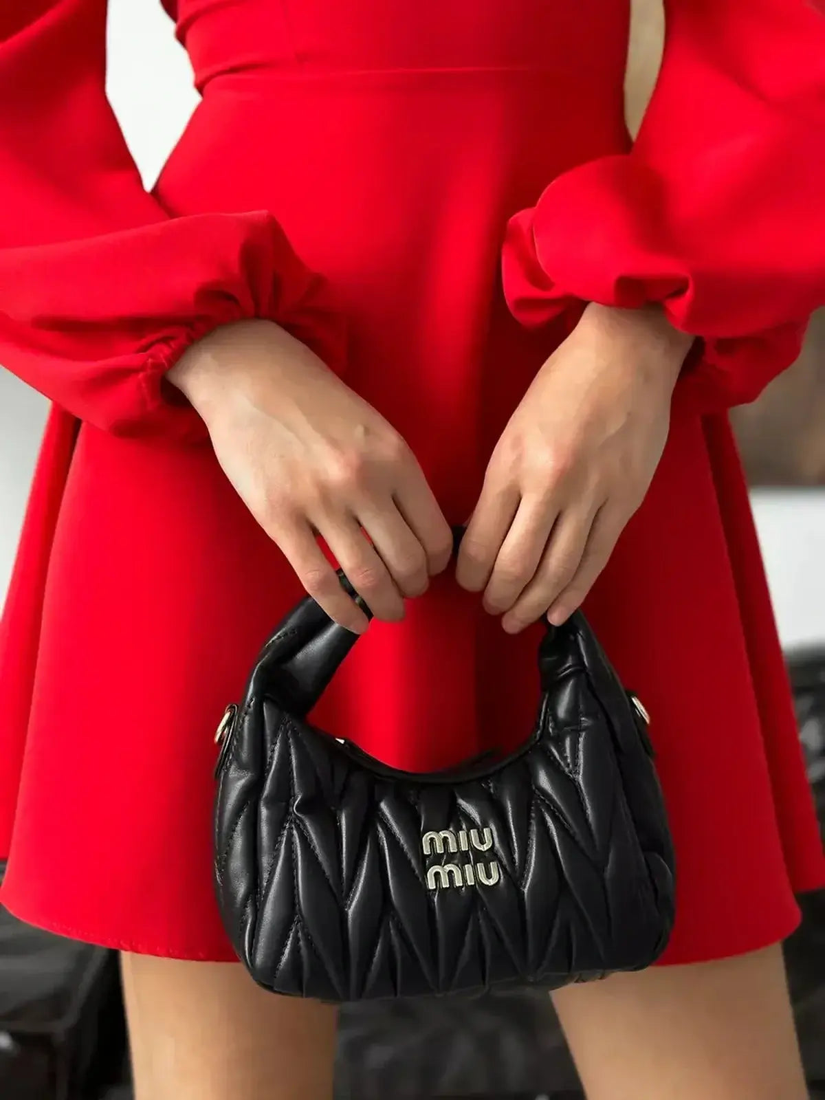 Model wearing a red mini dress holding a trendy black Miu Miu handbag, showcasing chic women clothing.