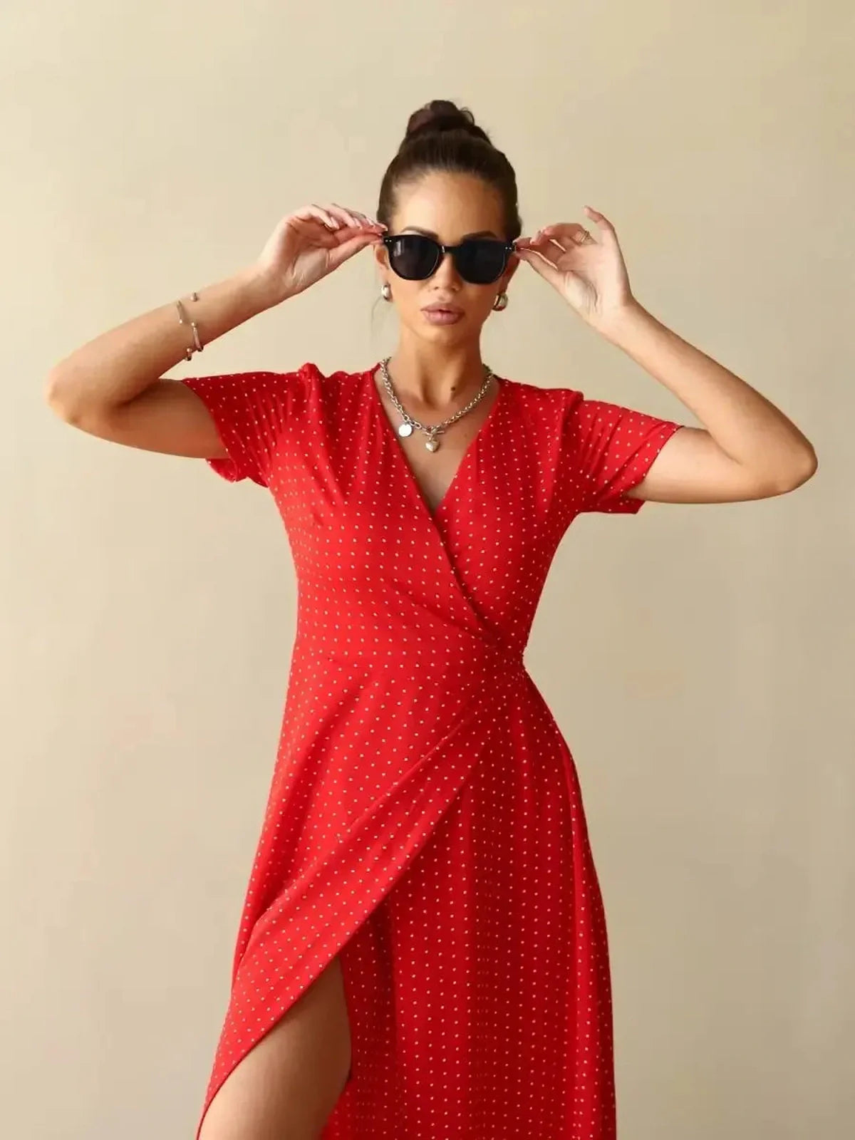 Woman wearing Ruby Grace Maxi Dress in red polka dots, showcasing V-neckline and side slit, styled with sunglasses.