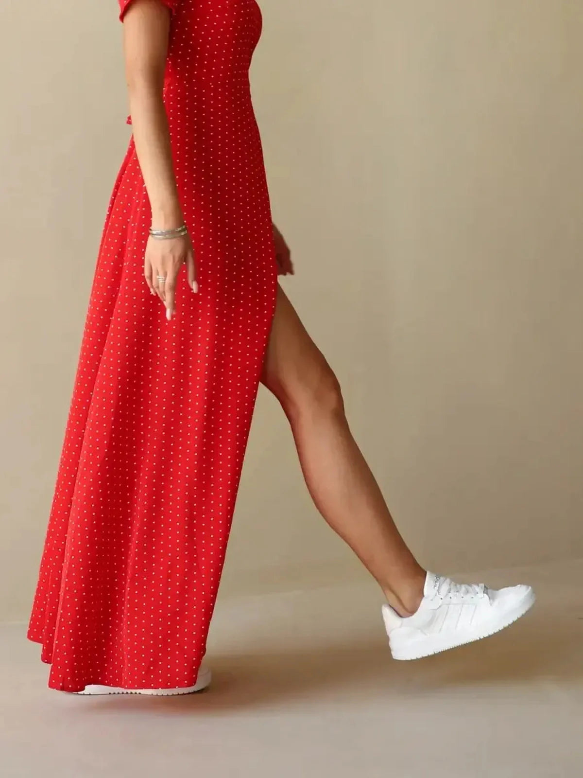 Woman wearing a Ruby Grace Maxi Dress in vibrant red polka dots with a side slit and white sneakers.