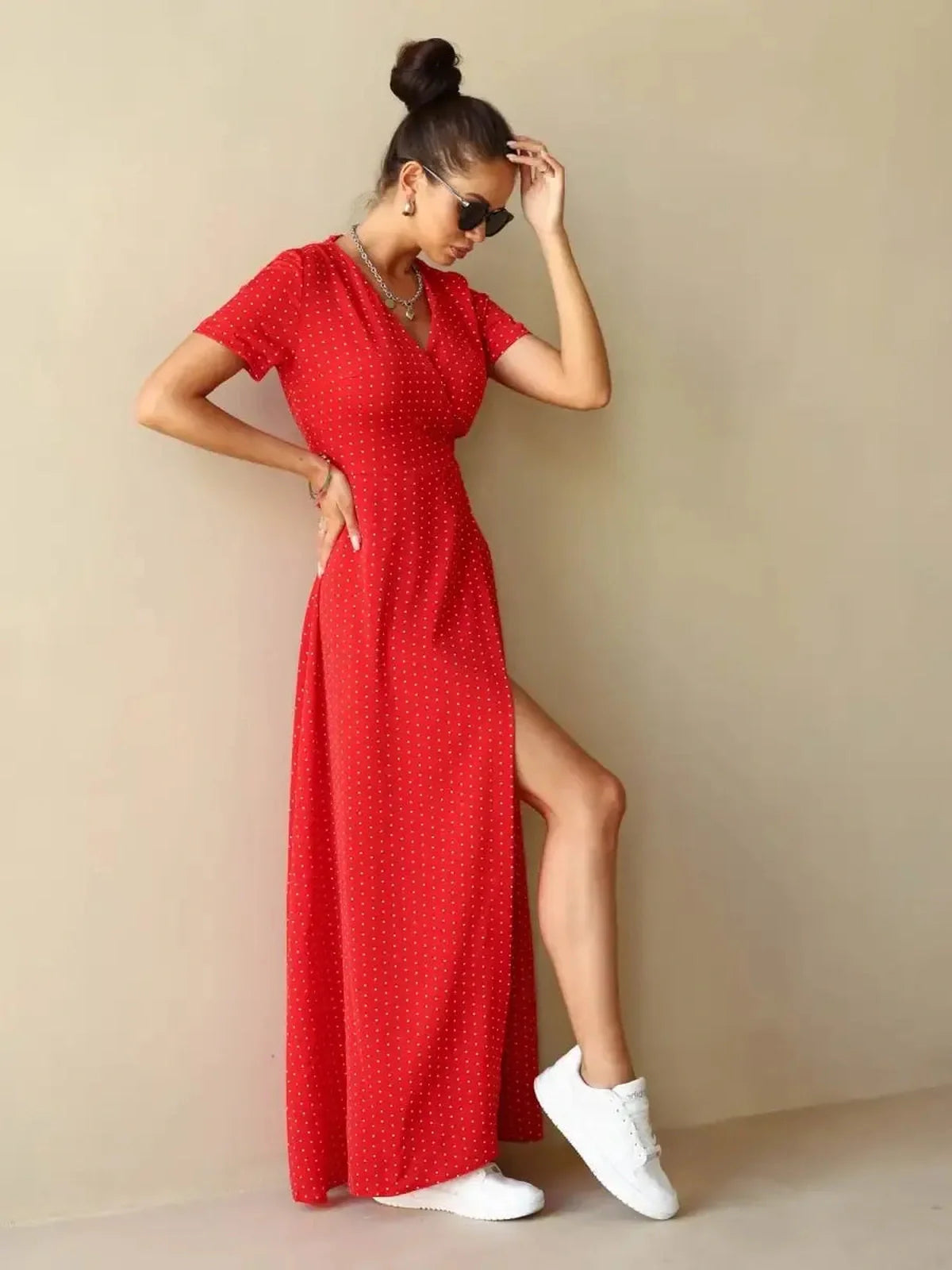 Model wearing a Ruby Grace Maxi Dress in red polka dots with a V-neckline and side slit, paired with white sneakers.