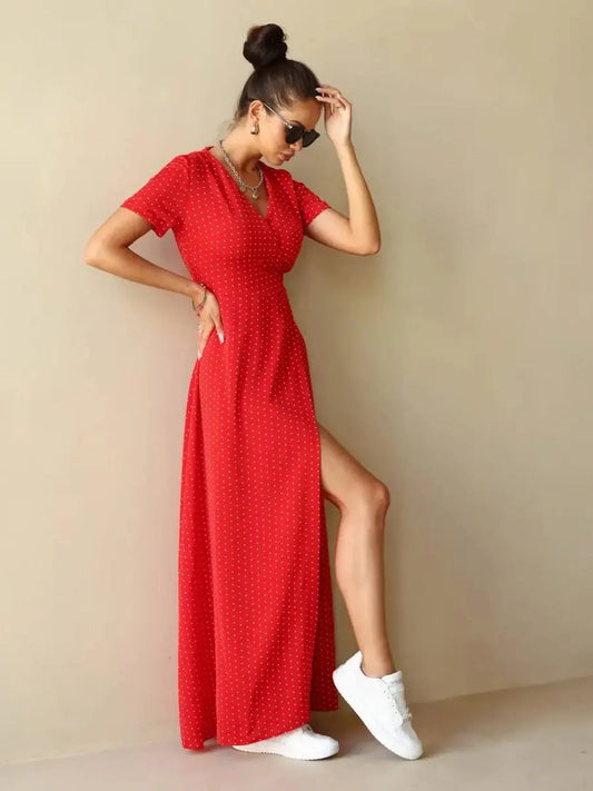 Model wearing a Ruby Grace Maxi Dress in red polka dots with a V-neckline and side slit, paired with white sneakers.