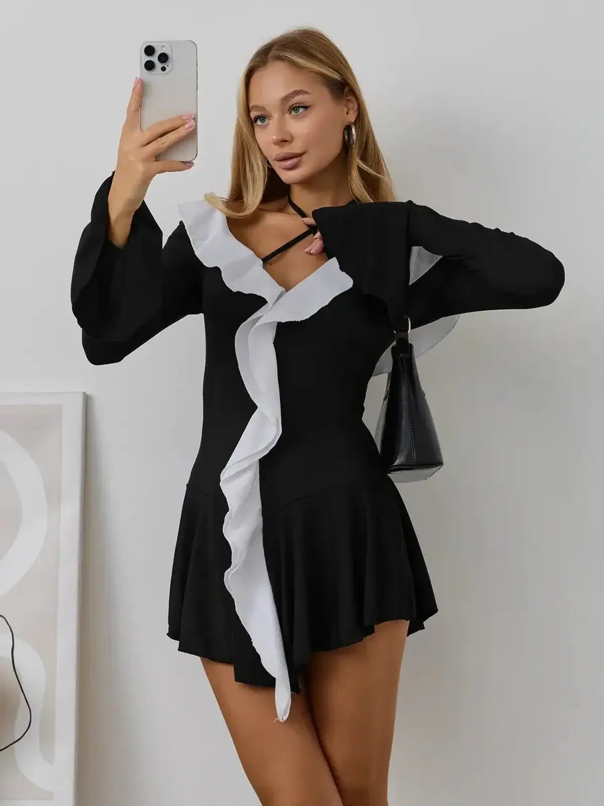 Model wearing the Ruffle Affair mini dress in black and white, showcasing long sleeves and flared cuffs.