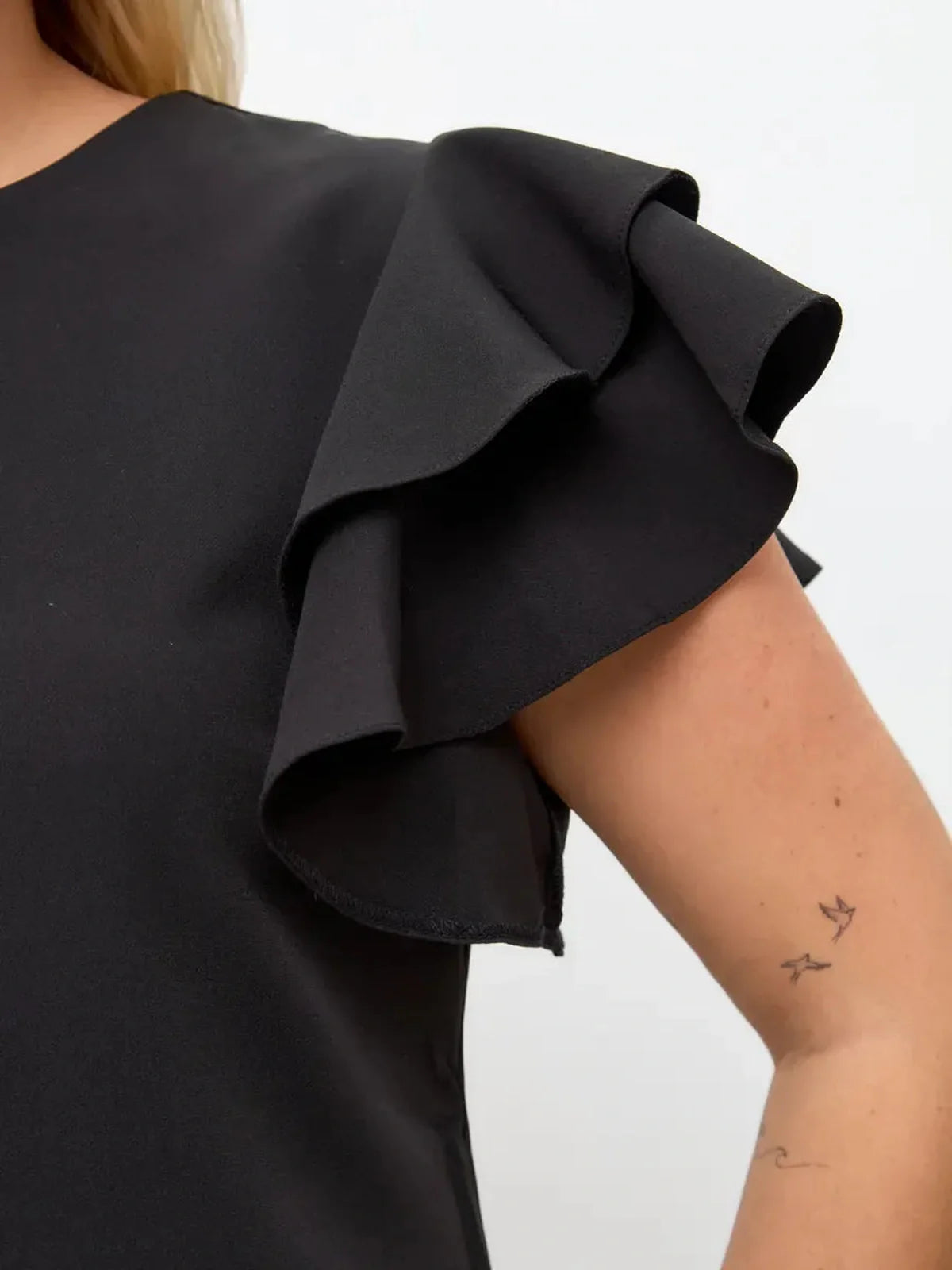 Close-up of layered ruffle sleeves on a black mini dress, showcasing elegant design and feminine movement.