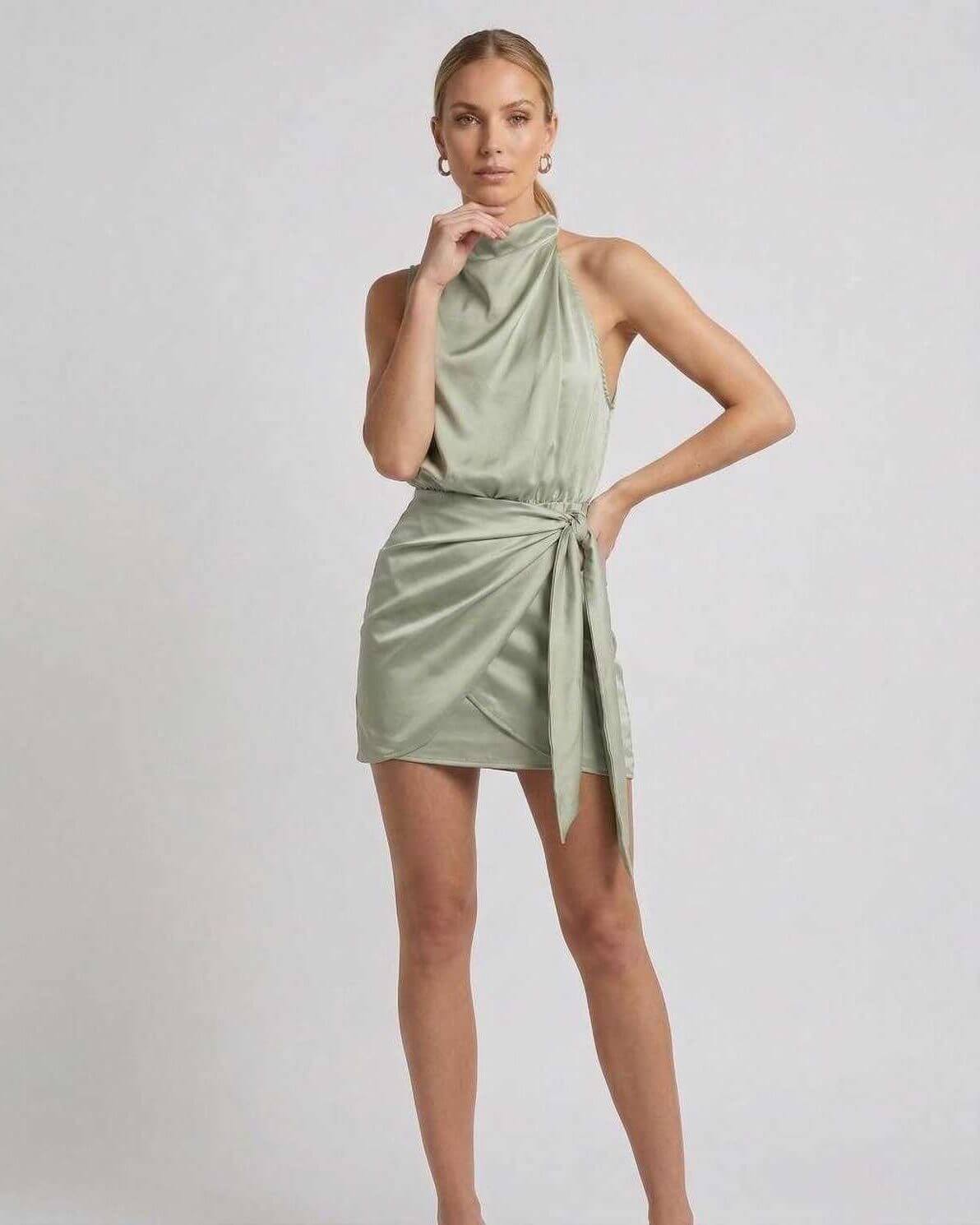 Sahara Mini Dress by Lauven featuring elegant satin fabric, draped high neck, and wrap tie detail in soft sage green.