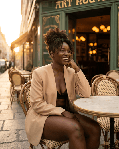 Savona Blazer by Lauven worn by a woman sitting at a café, showcasing a modern tailored silhouette in beige.