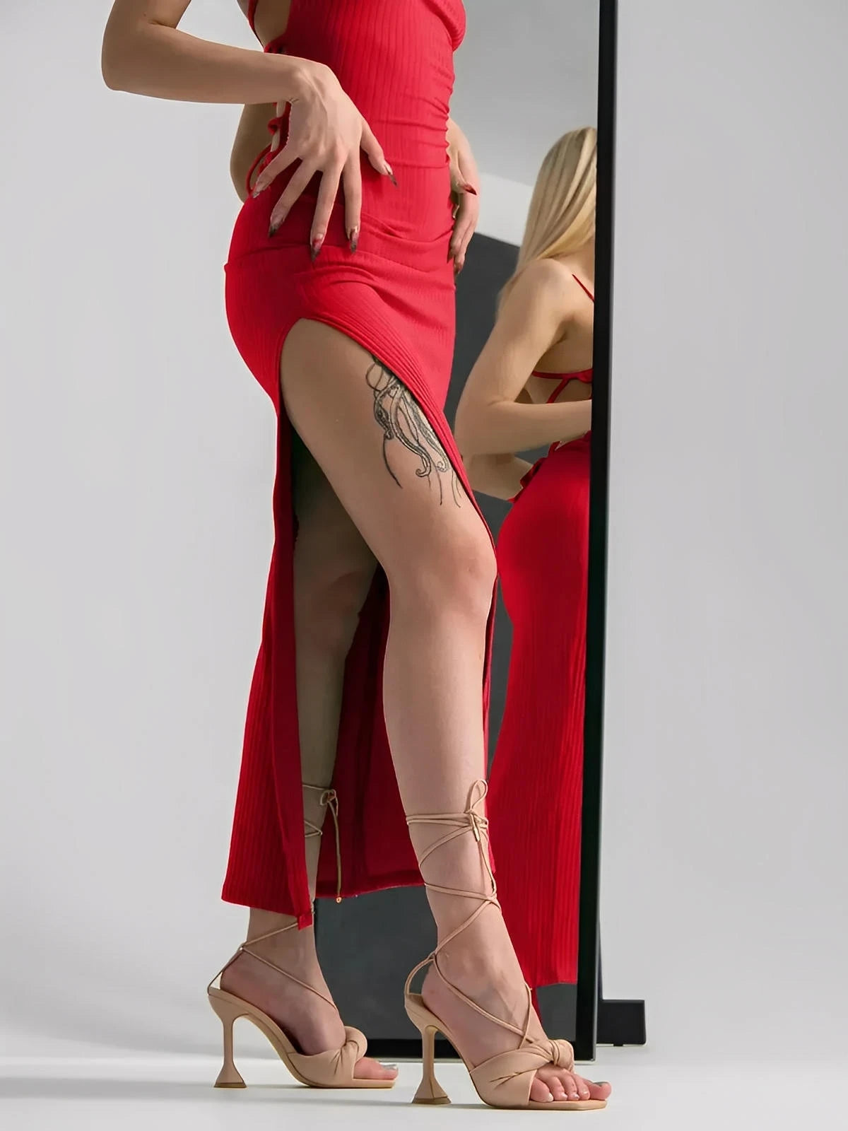 Model showcasing the Scarlet Lace Midi Dress with a thigh-high slit and elegant strappy sandals in front of a mirror.