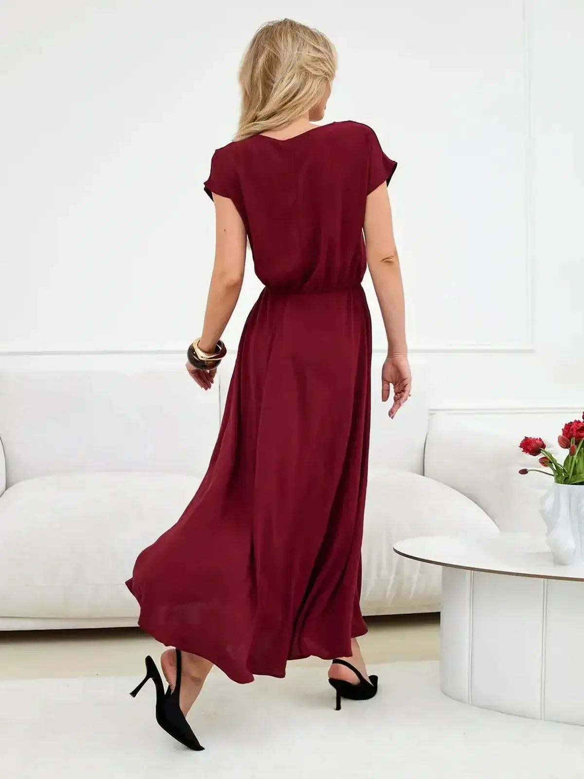Back view of a woman in a burgundy maxi dress with flowing skirt, showcasing elegant draping and a cinched waist.