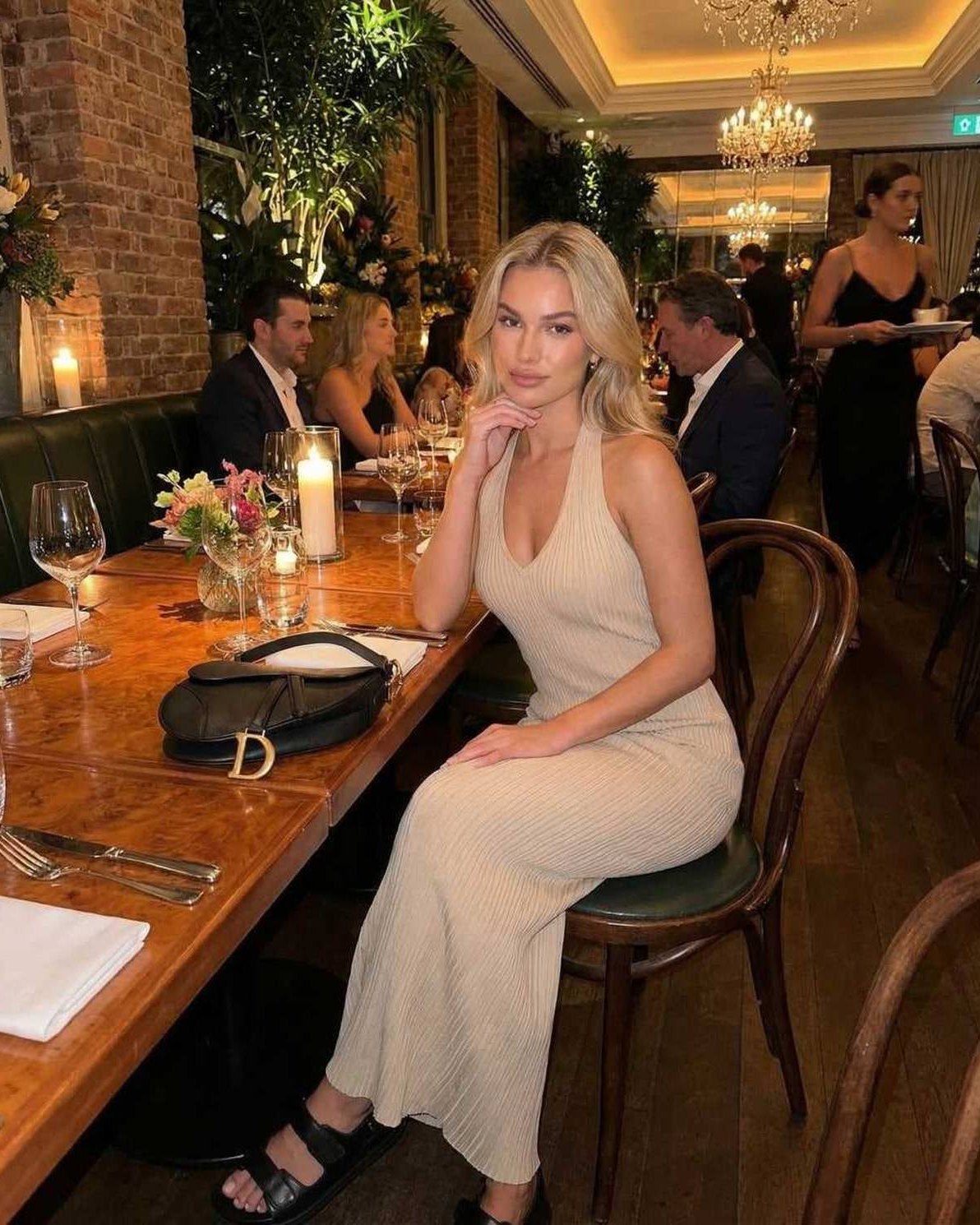 Woman wearing Serena Maxi Dress by Lauven at a classy dining setting, showcasing elegant ribbed knit design in beige.
