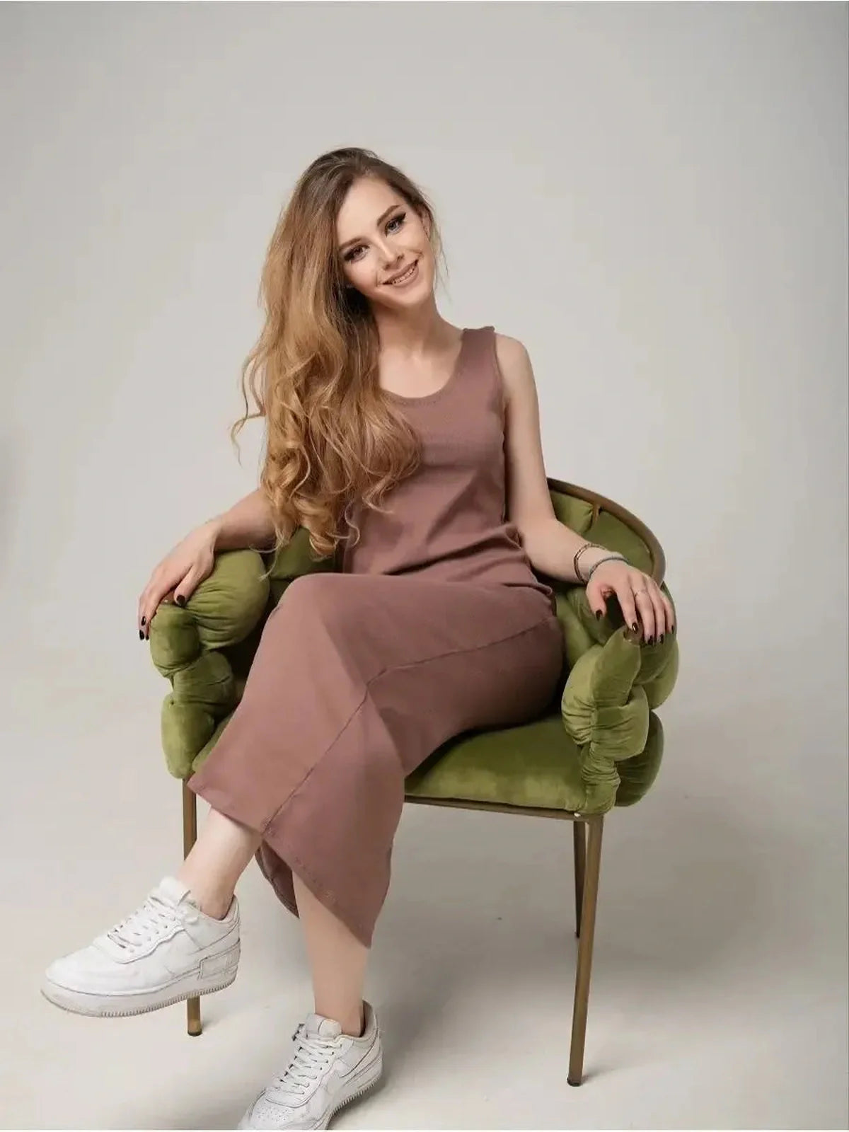 Stylish woman wearing Serene Flow Maxi Dress in soft fabric, seated gracefully on a green chair.