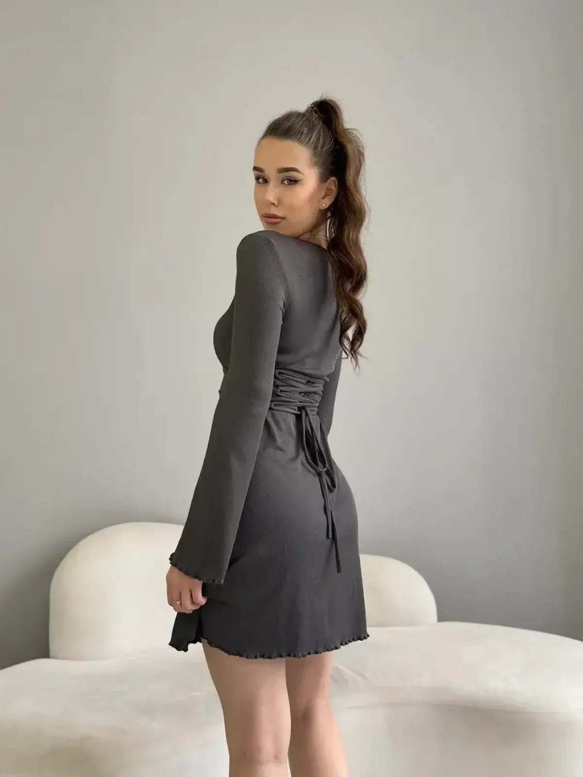 Stylish woman wearing a figure-defining black mini dress with a square neckline and long sleeves.