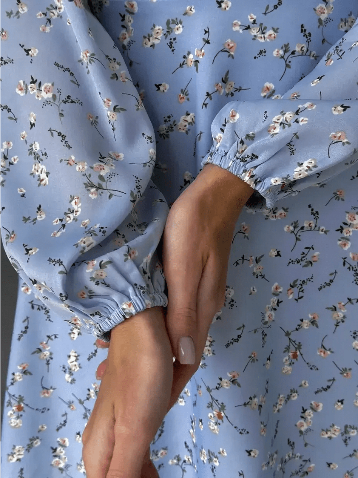 Close-up of hands in a floral sky blue mini dress with puffed sleeves, showcasing breezy elegance and feminine style.
