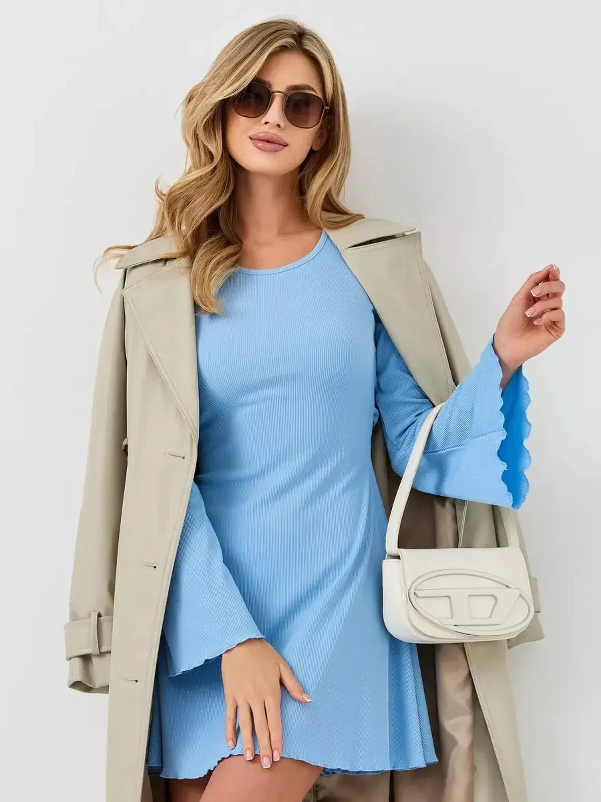 Model wearing a light blue Skyline Flare mini dress with flared sleeves and sunglasses, styled with a trench coat.