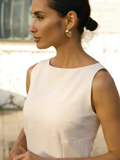 Close-up of a woman in a sleeveless white mini dress showcasing a round neckline, perfect for summer and wedding guest events.
