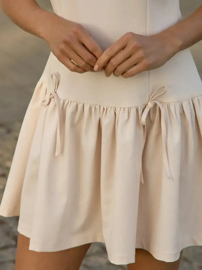 Close-up of a soft beige mini dress with flared skirt and decorative ties, perfect for summer or wedding events.