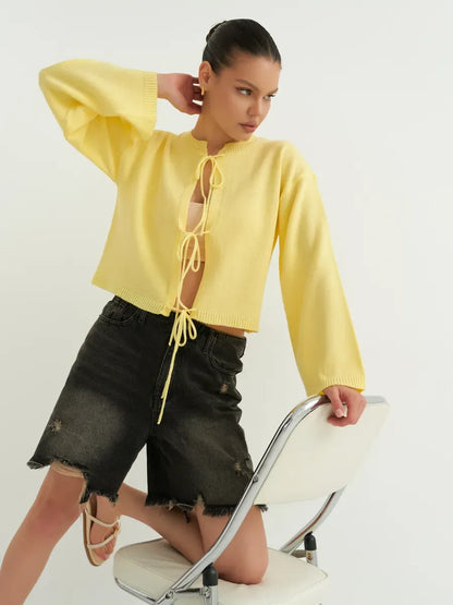 Model wearing a cropped yellow knit Solara Cardigan by Lauven with tie-front detailing.