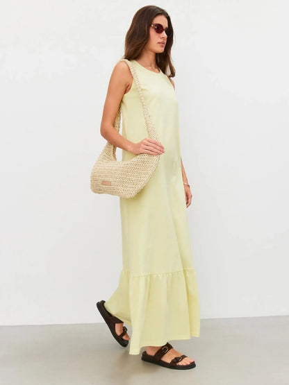 Model wearing a sleeveless lemon yellow Sunrise Maxi Dress, styled with a woven bag and sandals.