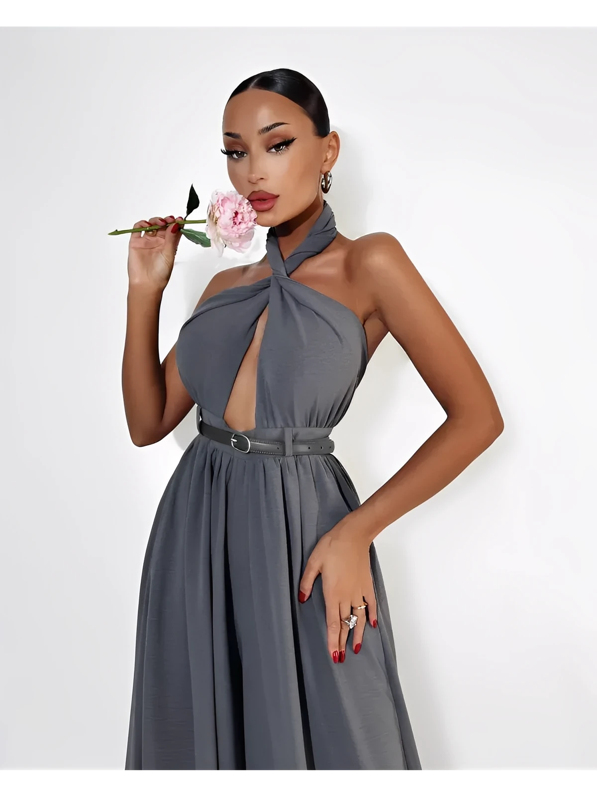 Woman wearing a grey Twist Halter Jumpsuit with open back and wide legs, posing with a flower.