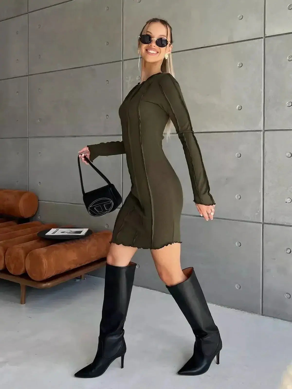 Olive green long sleeve mini dress with contrast stitching, styled with knee-high boots and sunglasses.