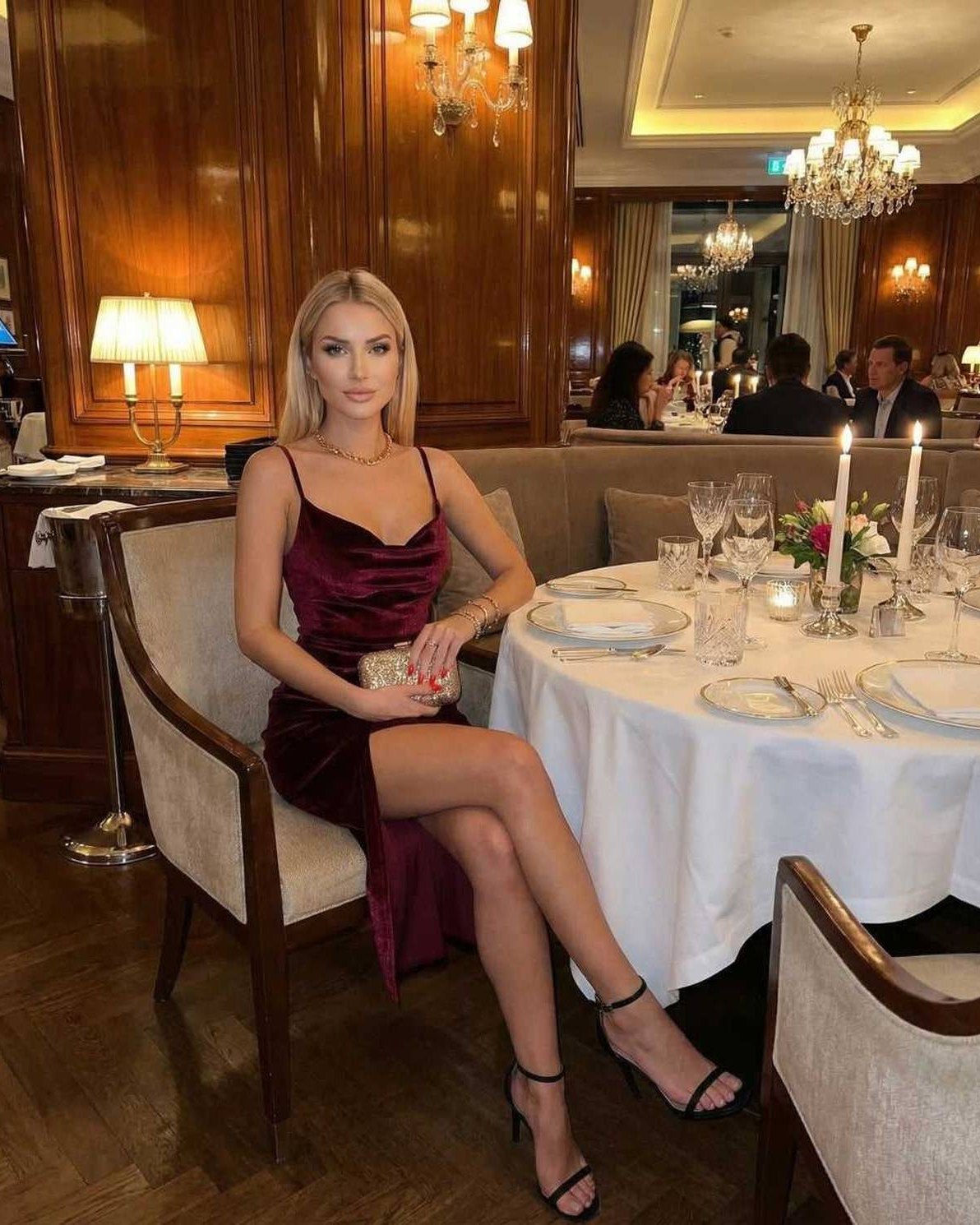Woman wearing Vega Midi Dress by Lauven, a luxurious velvet sheath with side slit, in an elegant dining setting.