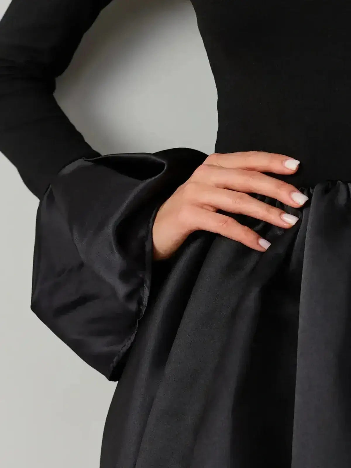 Close-up of a hand on a black velvet dress featuring a satin balloon skirt and exaggerated cuffs.