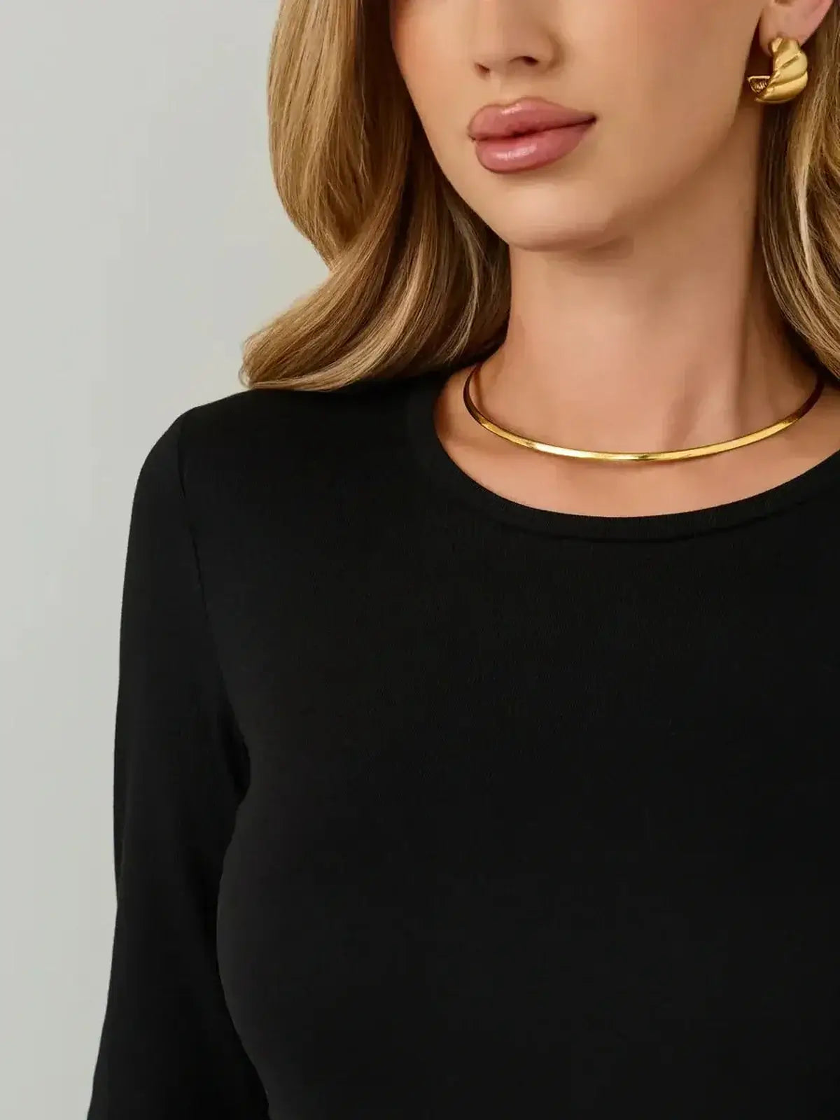 Close-up of a model wearing a black dress with a rounded neckline and gold jewelry for a stylish look.