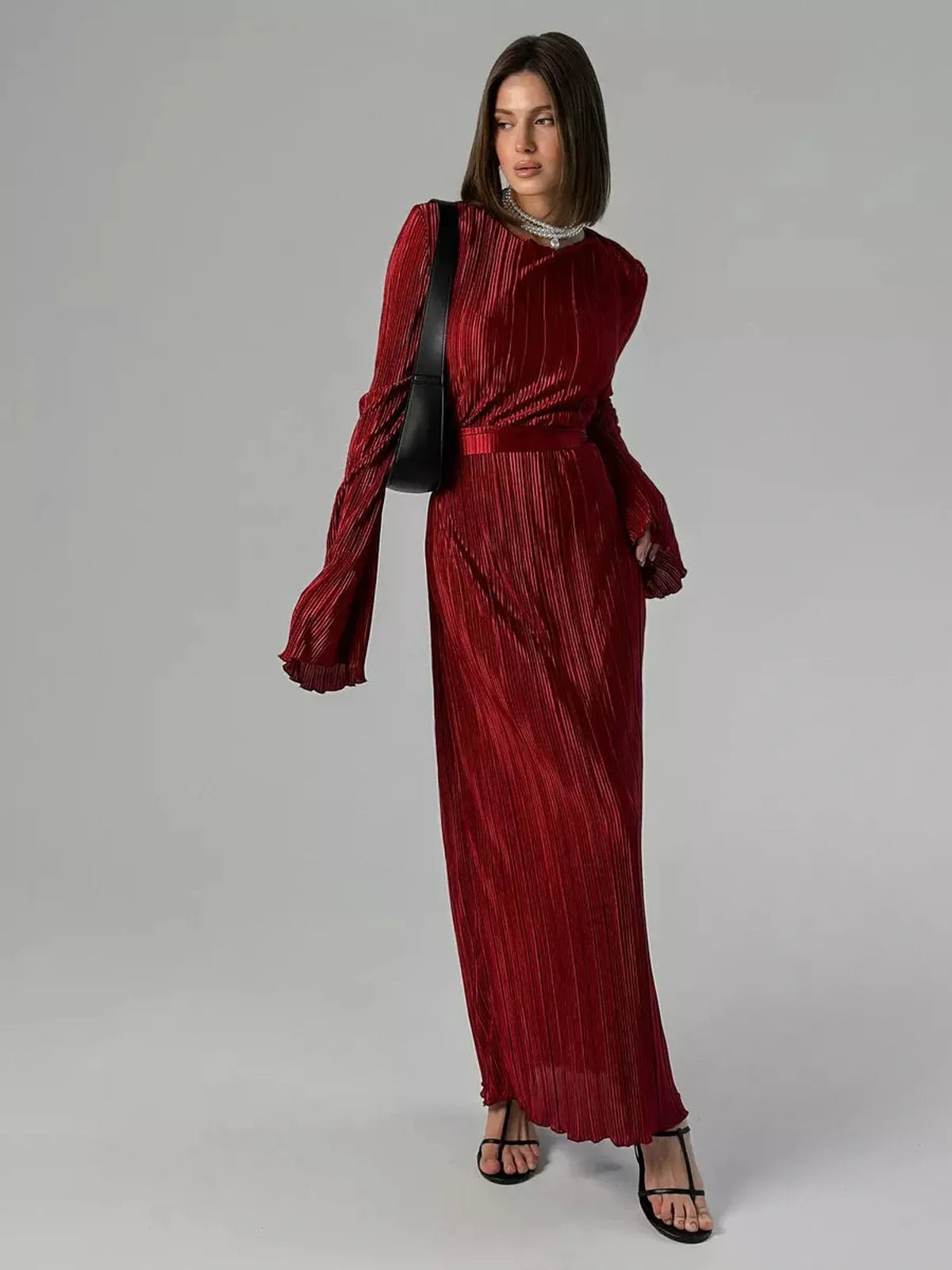 Model showcases the Velvet Flame Maxi Dress in glossy marsala red with flared sleeves and pleated fabric, ideal for formal occasions.