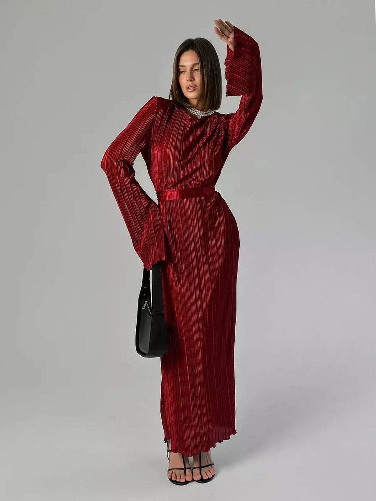 Model showcasing the Velvet Flame Maxi Dress in glossy marsala red, featuring pleats and flared sleeves.