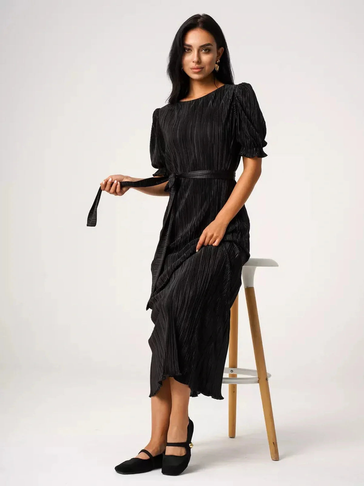Model wearing a black Velvet Rhythm Maxi Dress with puff sleeves and a detachable sash belt, showcasing a pleated design.