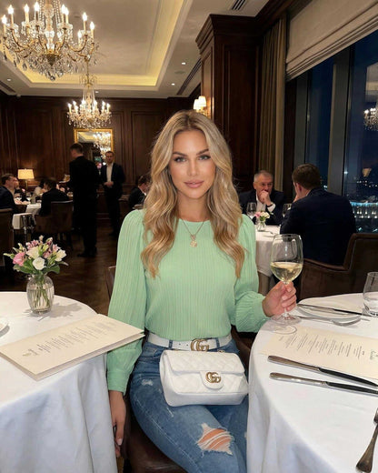 Verde Blouse by Lauven worn by a woman in a restaurant, featuring fresh green pleated long sleeves and stylish denim.