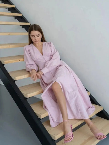 Model wearing the Willow Grace Maxi Dress in soft pink, featuring a plunging neckline and long sleeves on a staircase.