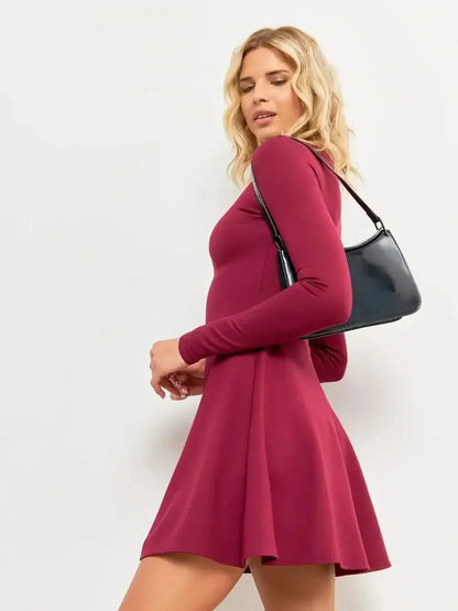 Model wearing the Wine Flare Mini dress in burgundy, featuring long sleeves and a flared hem, styled with a black handbag.