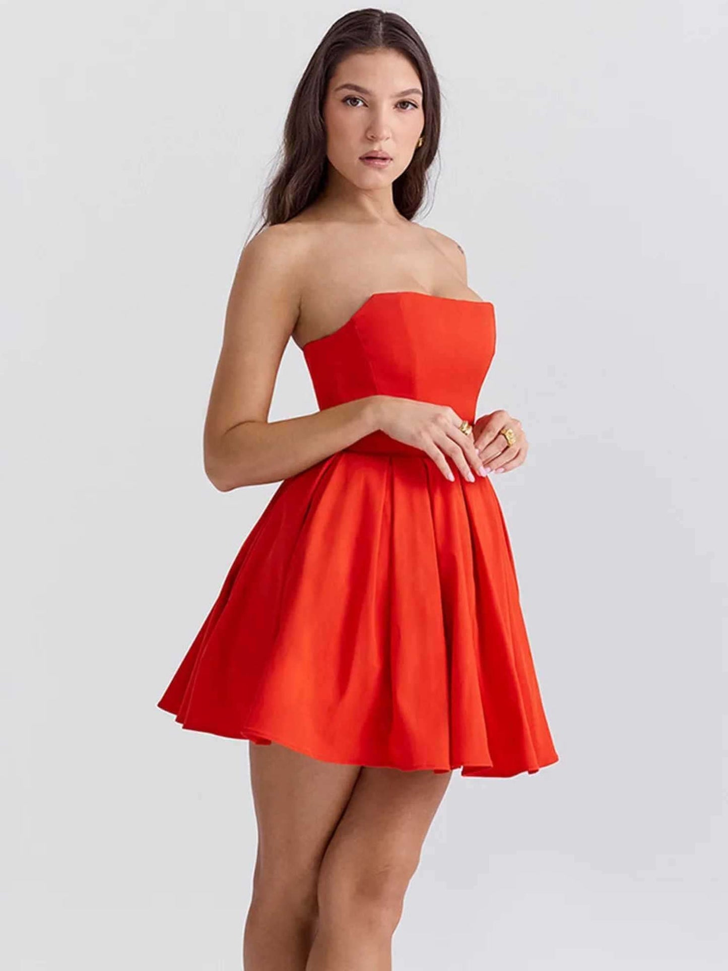 Model wearing a vibrant red strapless mini dress with a pleated skirt, ideal for summer or party occasions.